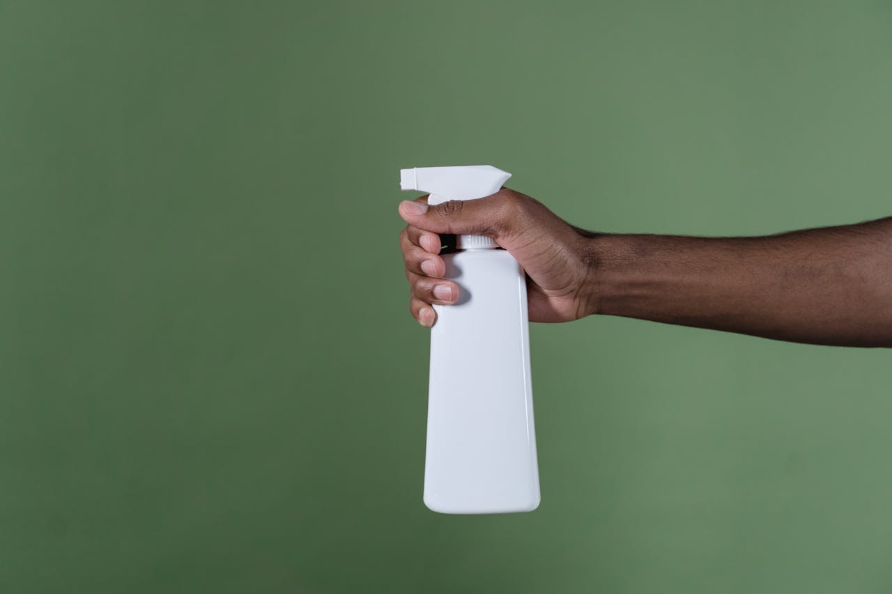 about-02 A hand holds a white spray bottle against a green background, perfect for cleaning product concepts.